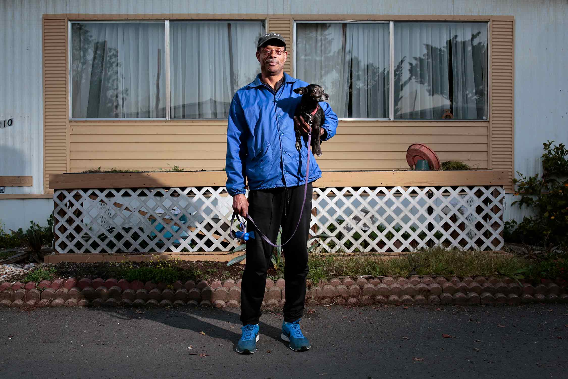 photo of a man holding a dog in front of a home
